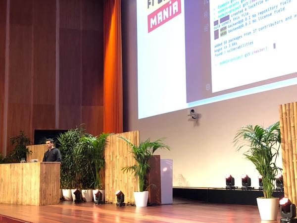 On a large stage decorated with bamboos and plants, Andre Staltz is looking at this computer while he gives a technical talk about programming; behind and above him you can see a large projected screen where slides are shown