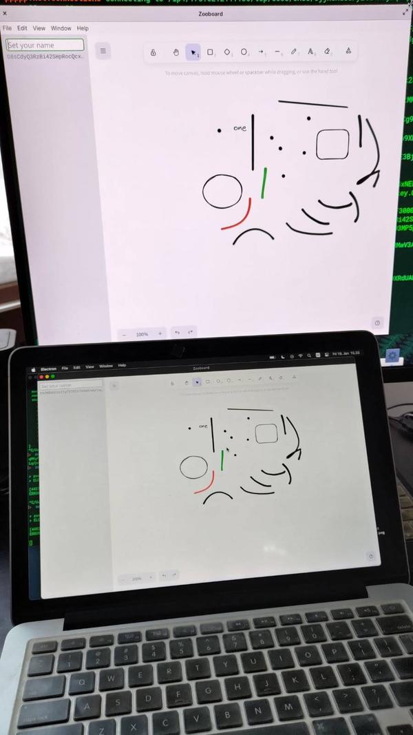 Photograph of two computers where they are both displaying a whiteboard app on the screen, with the exact same drawings